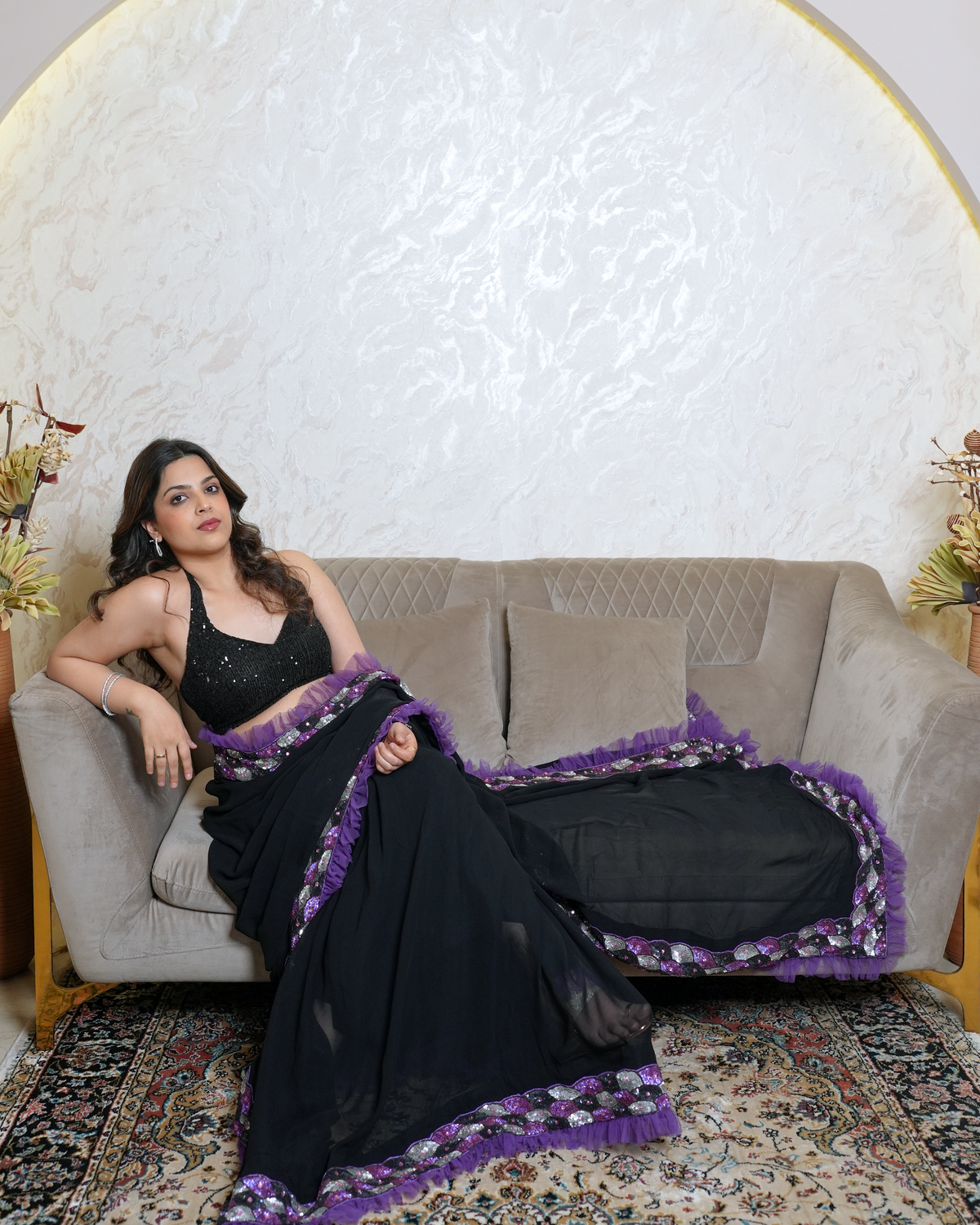 Zaria by House of Somarra — Seated view with the black saree and purple-bordered pallu spread across the sofa.