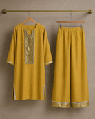 Aabha gold-mustard linen shirt and palazzo displayed separately on hangers, showing mirror-lace and antique-shimmer details.