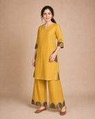 Three-quarter view of the Arpita golden-mustard linen co-ord, showing the semicircle patch work on the shirt pockets and sleeves