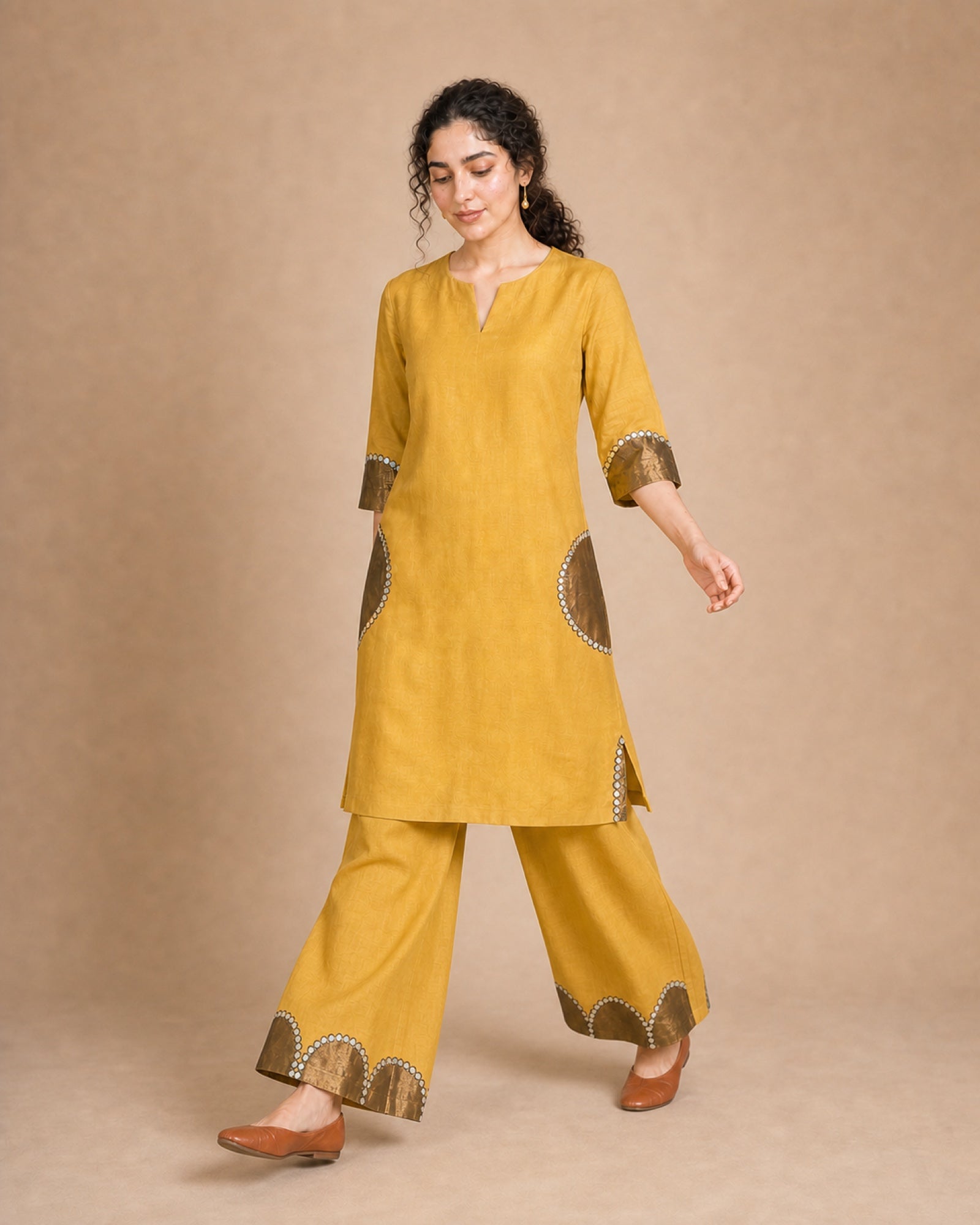 Front three-quarter view of the Arpita golden-mustard linen co-ord, with semicircle antique-shimmer and mirror-lace treatment visible on the sleeve and palazzo