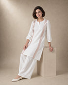 Three-quarter view of the Aurelle white linen co-ord set, showing the rose-gold-colour front trim and matching broad palazzos
