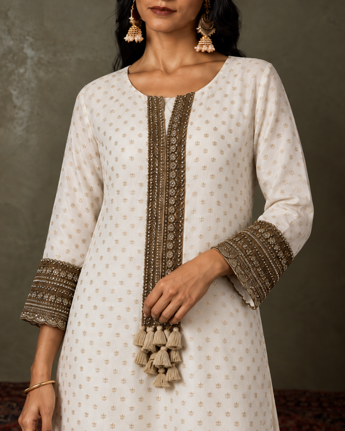 Hemika — close-up of ivory kurta buti, antique-gold borders and tassel detail